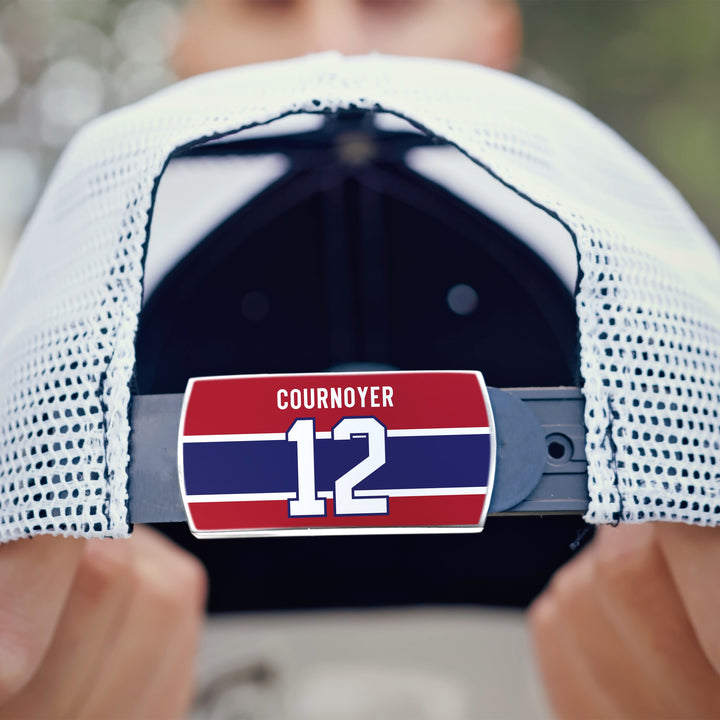 A person holds a white mesh ZippyBack™ baseball cap backward, revealing a red, blue, and white strap tag with the name Yvan Cournoyer—celebrating hockey speed and legacy.