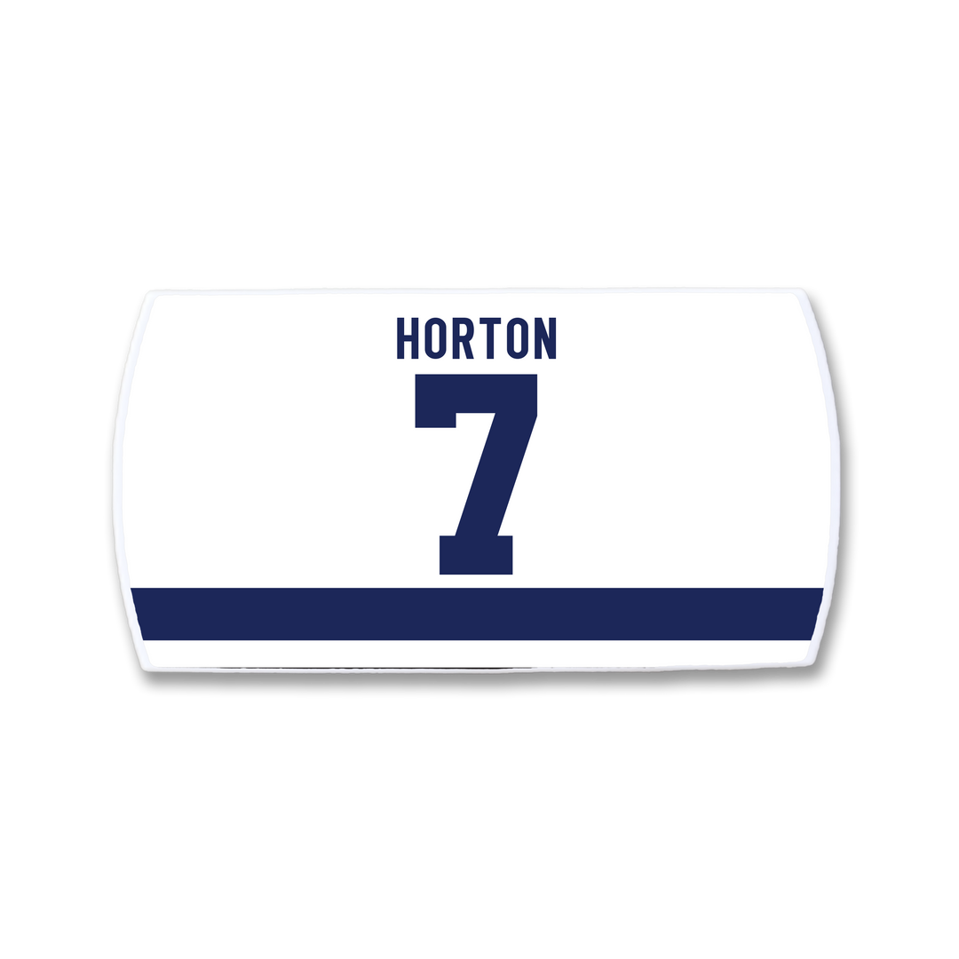 A white rectangular ZippyBack™ sports jersey nameplate features a bold navy blue number 7 with "HORTON" above and a horizontal navy stripe below—celebrating Tim Horton&