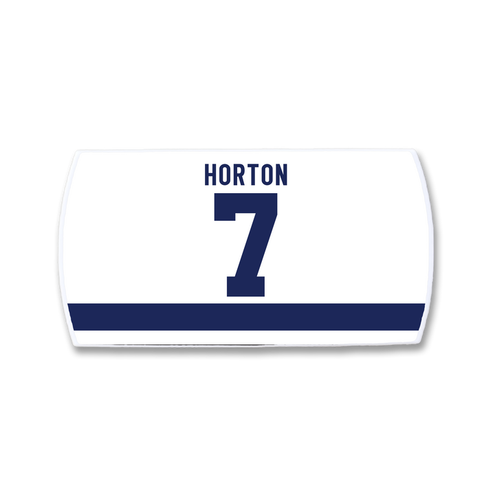 A white rectangular ZippyBack™ sports jersey nameplate features a bold navy blue number 7 with "HORTON" above and a horizontal navy stripe below—celebrating Tim Horton&