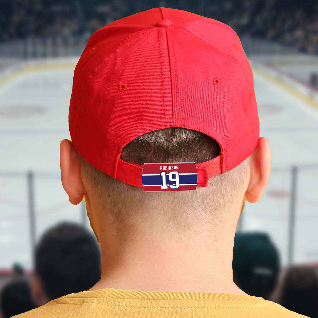 A person wearing a red baseball cap, viewed from behind, with a hockey arena in the background. The cap has a tag with the name Robinson and the number 19 in white and red on a blue and red background.