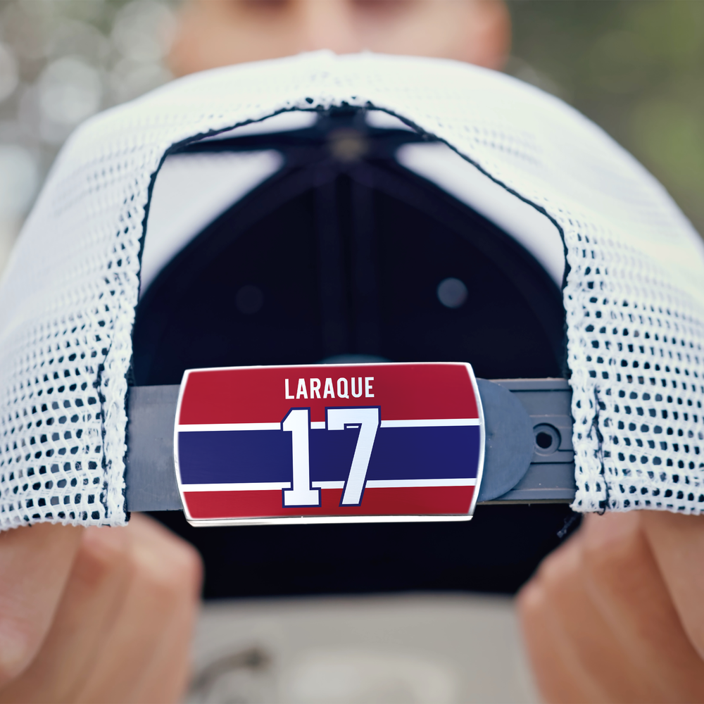 A person holds a white mesh ZippyBack™ baseball cap featuring a red, blue, and white Georges Laraque label on the strap—symbolizing heavyweight strength and discipline—against a blurred green tree background.