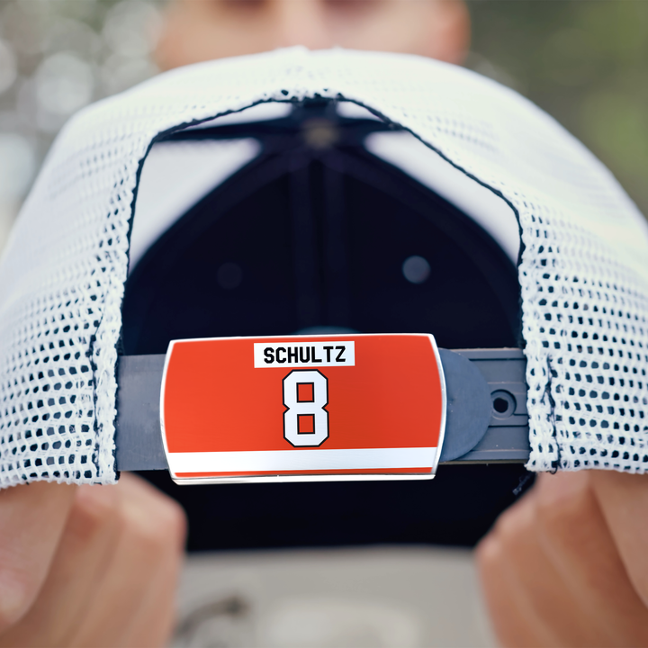 A person holds a white mesh baseball cap by ZippyBack™, featuring an adjustable strap with a red Dave Schultz label and the number 8—a tribute to his momentum and physical play.