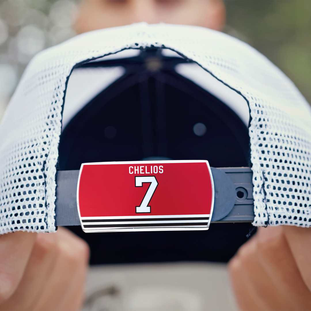 A person holds the back of a white mesh ZippyBack™ Chris Chelios cap featuring a red CHELIOS 7 label with black stripes, inspired by legendary defenseman Chris Chelios’s iconic hockey jersey.
