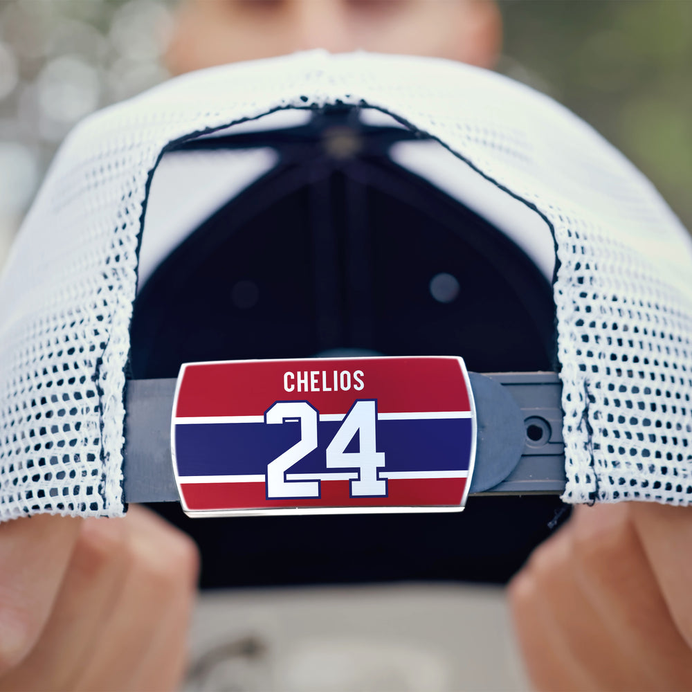 A close-up of a durable ZippyBack™ Chris Chelios mesh baseball cap held backward, highlighting the red, white, and blue strap tag with "Chelios" and the number 24 against a blurred background.