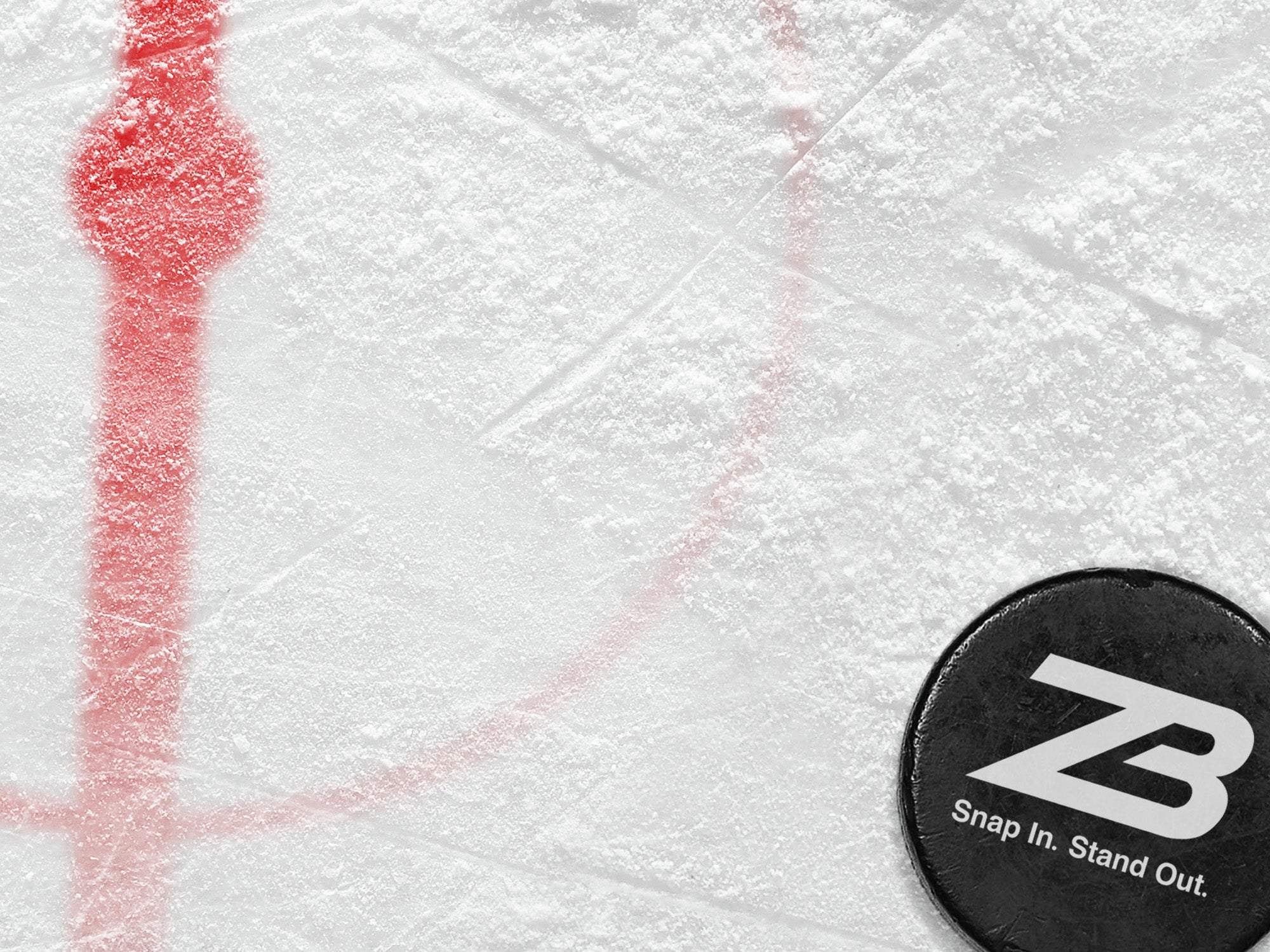 A black hockey puck with white ZB logo and the text Snap In. Stand Out. rests on an ice rink near a red faceoff circle and line.