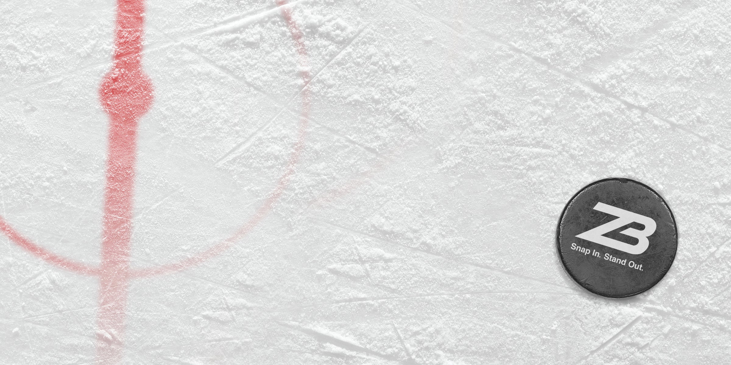A hockey puck with the ZB logo and the text Snap In. Stand Out. rests on scratched ice near a red faceoff circle marking.