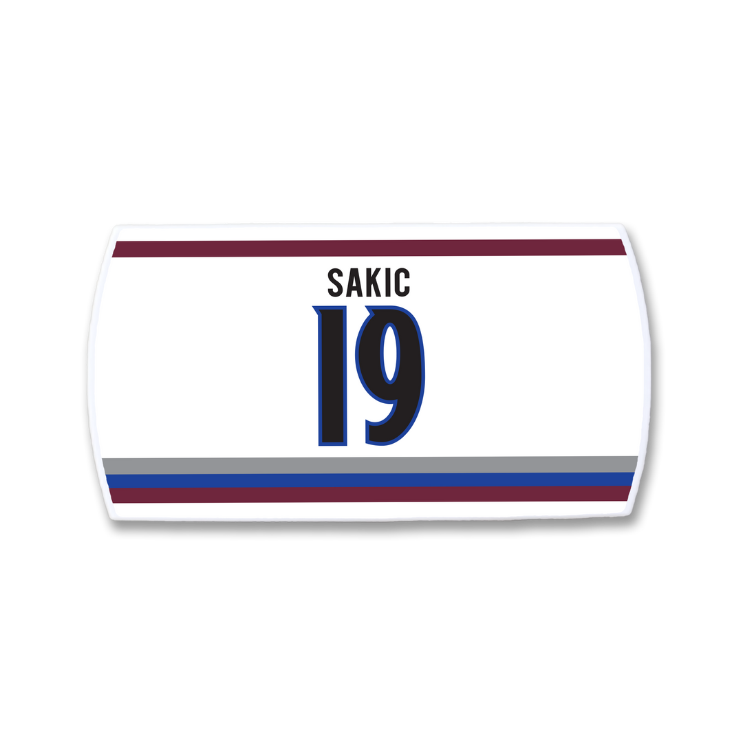 The ZippyBack™ Joe Sakic white hockey jersey nameplate features SAKIC above number 19 in blue/black, bordered by maroon, blue, and gray stripes—a tribute to his elite vision and legendary play.