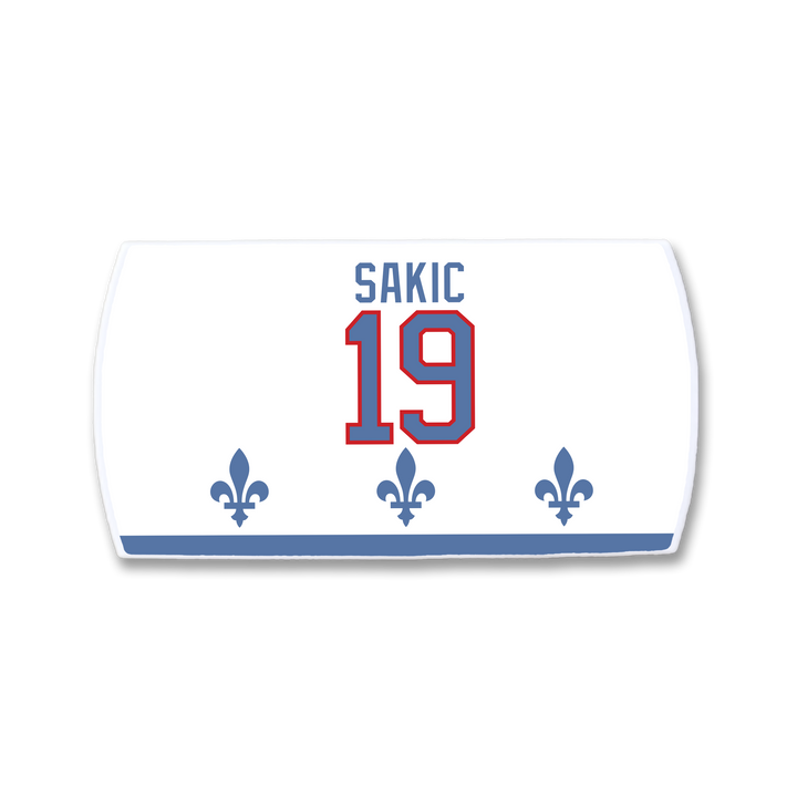 The ZippyBack™ Joe Sakic white hockey jersey nameplate features “SAKIC” in blue above red number 19, three blue fleur-de-lis below, and a blue stripe at the bottom—honoring the legendary player.