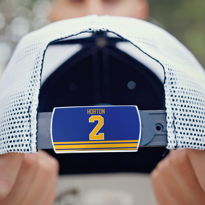 A person holds the back of a white mesh ZippyBack™ cap. Its adjustable strap has a blue tag reading "Tim Horton" and displays the number 2 in yellow above two yellow stripes. The person&