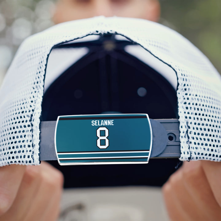 A person holds a ZippyBack™ Teemu Selänne white mesh baseball cap, displaying its adjustable strap with a teal label reading "SELANNE 8" in white—honoring hockey legend Teemu Selänne.