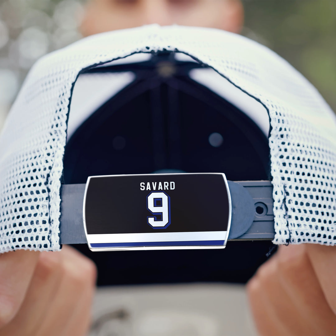 A close-up shows the back of a white mesh ZippyBack™ cap featuring a black label with "Denis Savard" and the number 9 in white. Someone holds the cap, their face blurred.