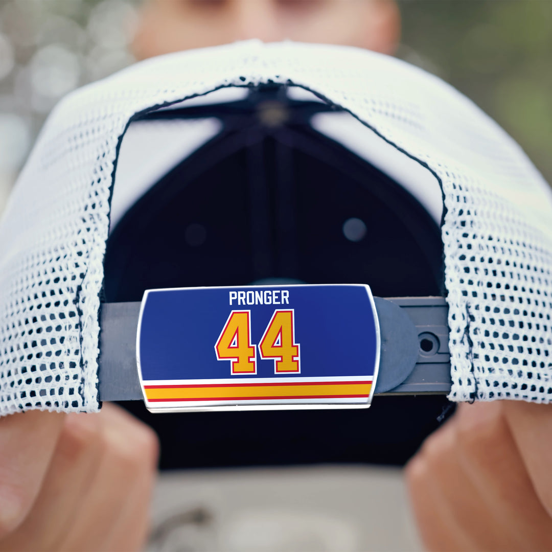 A person holds a white mesh ZippyBack™ Chris Pronger cap backwards, revealing a blue PRONGER 44 tag on the adjustable strap, accented by red, yellow, and white stripes underneath.
