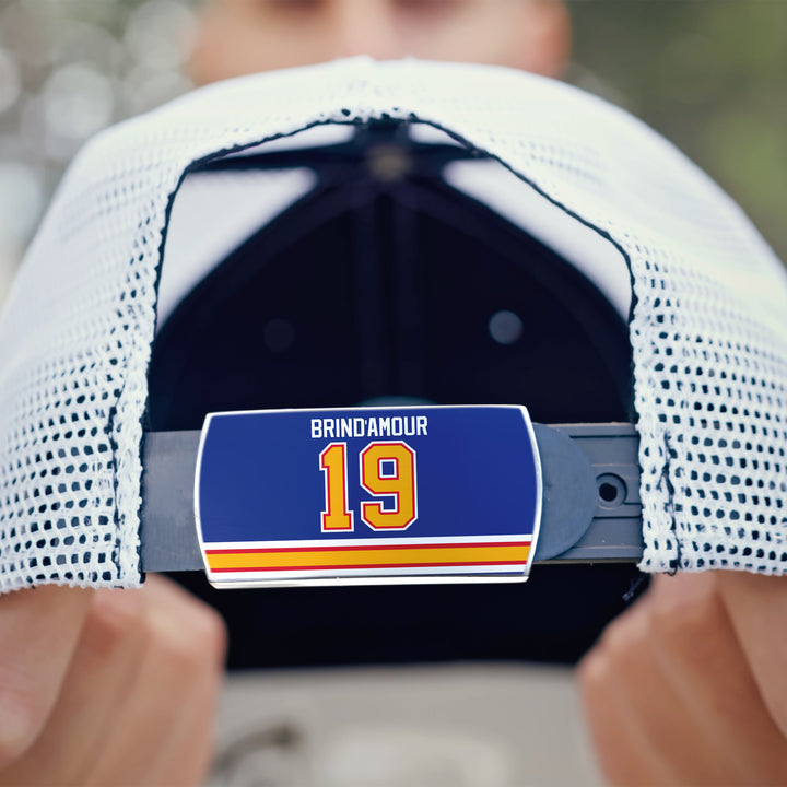 A person holds a white ZippyBack™ mesh baseball cap featuring an adjustable back strap with a blue label reading "Rod Brind’Amour 19" above red and yellow stripes, honoring the legendary two-way center.