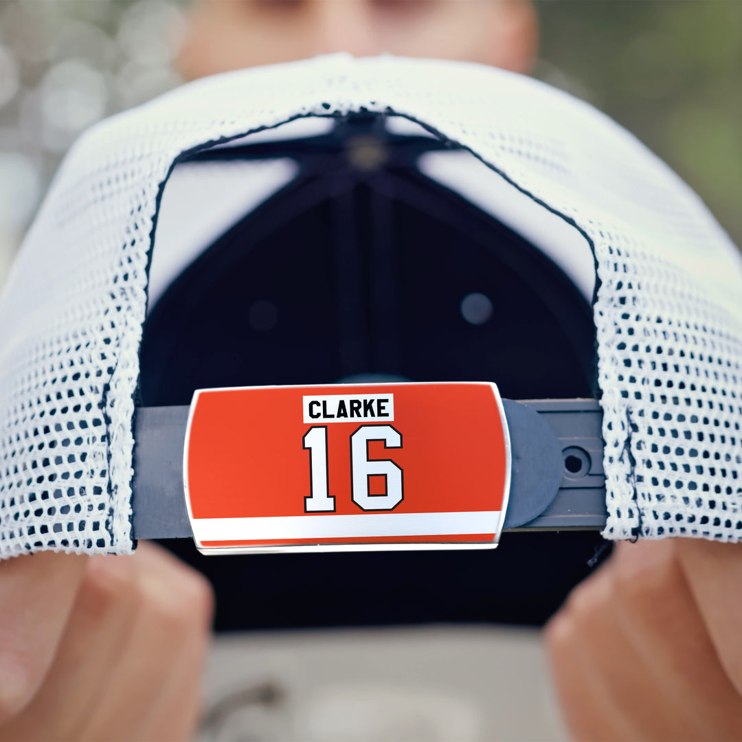 Close-up of the back of a white mesh ZippyBack™ cap featuring a red label with "Bobby Clarke" and number 16 in white and black, held in someone&