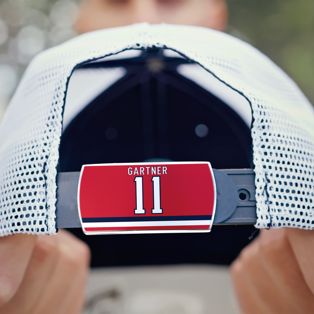 A person holds a white ZippyBack™ mesh cap backwards, displaying a red label on the adjustable strap that reads Mike Gartner in white letters above two white stripes—paying tribute to his legendary speed on the ice.