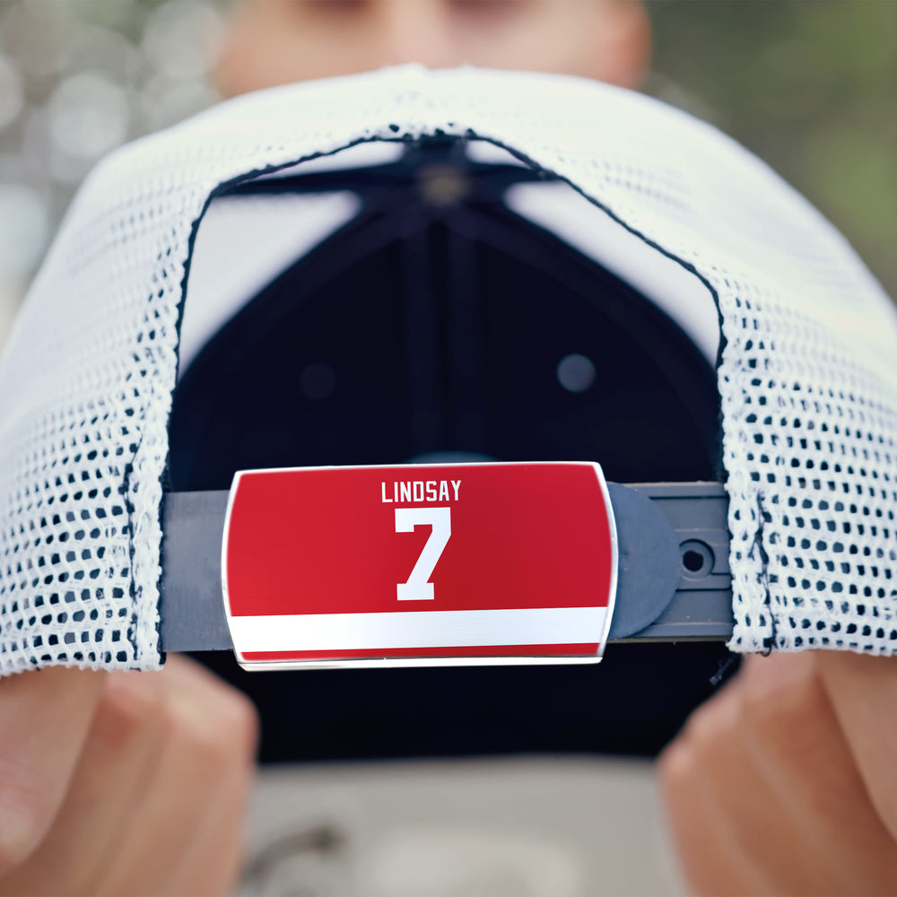 A close-up shows the back of a white mesh ZippyBack™ cap, featuring a red “Ted Lindsay” nameplate above a bold white number 7. Hands hold the hat, paying tribute to hockey legend Ted Lindsay against a softly blurred background.