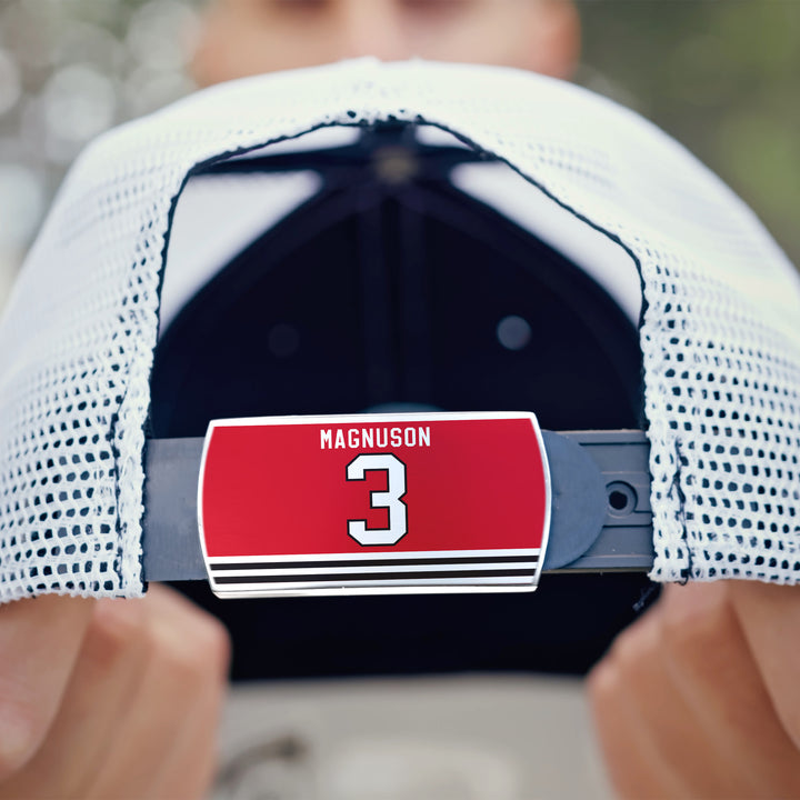 A close-up of the back of a white ZippyBack™ mesh baseball cap, featuring a red Keith Magnuson label and a white number 3 on the adjustable strap.