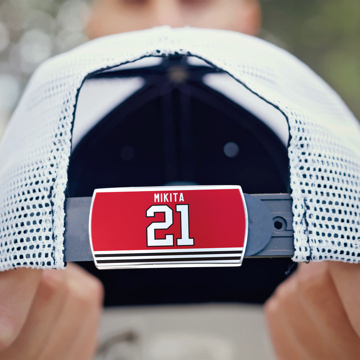 A person holds a white mesh baseball cap by ZippyBack™ named Stan Mikita, showing the back with a red tag that features "MIKITA 21" in bold white letters—a tribute to the legendary hockey player.