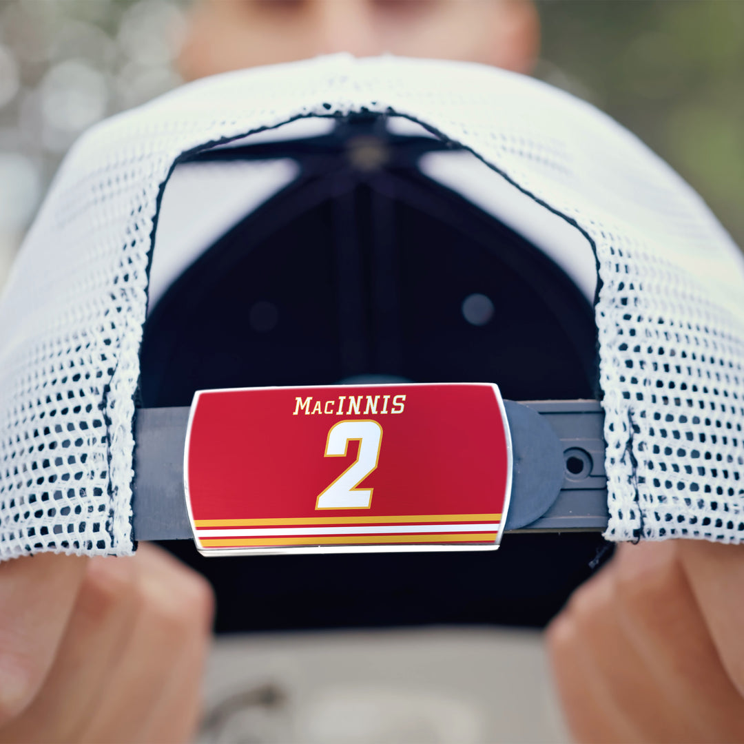 A person holds a white mesh ZippyBack™ cap, displaying its adjustable strap with a red label that reads "Al MacInnis 2"—honoring the legendary hockey player known for his powerful slapshot.