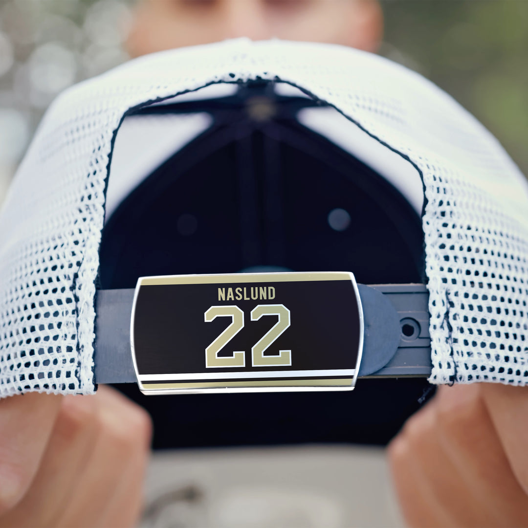 Close-up of the back of a white ZippyBack™ mesh cap, featuring an adjustable strap with a Markus Näslund label shown in bold text. A person holds the cap with both hands.