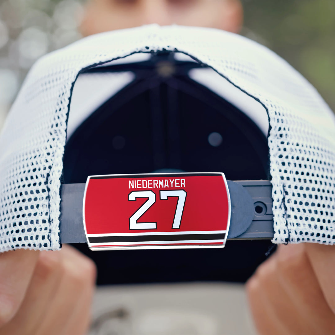 A person holds a white mesh ZippyBack™ cap featuring an adjustable strap with a red tag that reads Scott Niedermayer—honoring legendary hockey leadership.