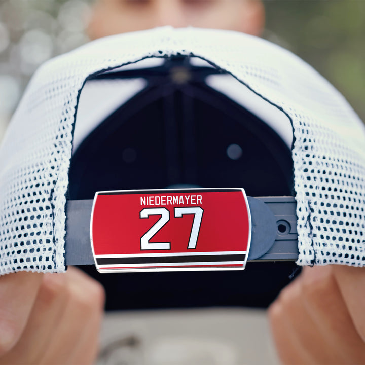 A person holds a white mesh ZippyBack™ cap featuring an adjustable strap with a red tag that reads Scott Niedermayer—honoring legendary hockey leadership.