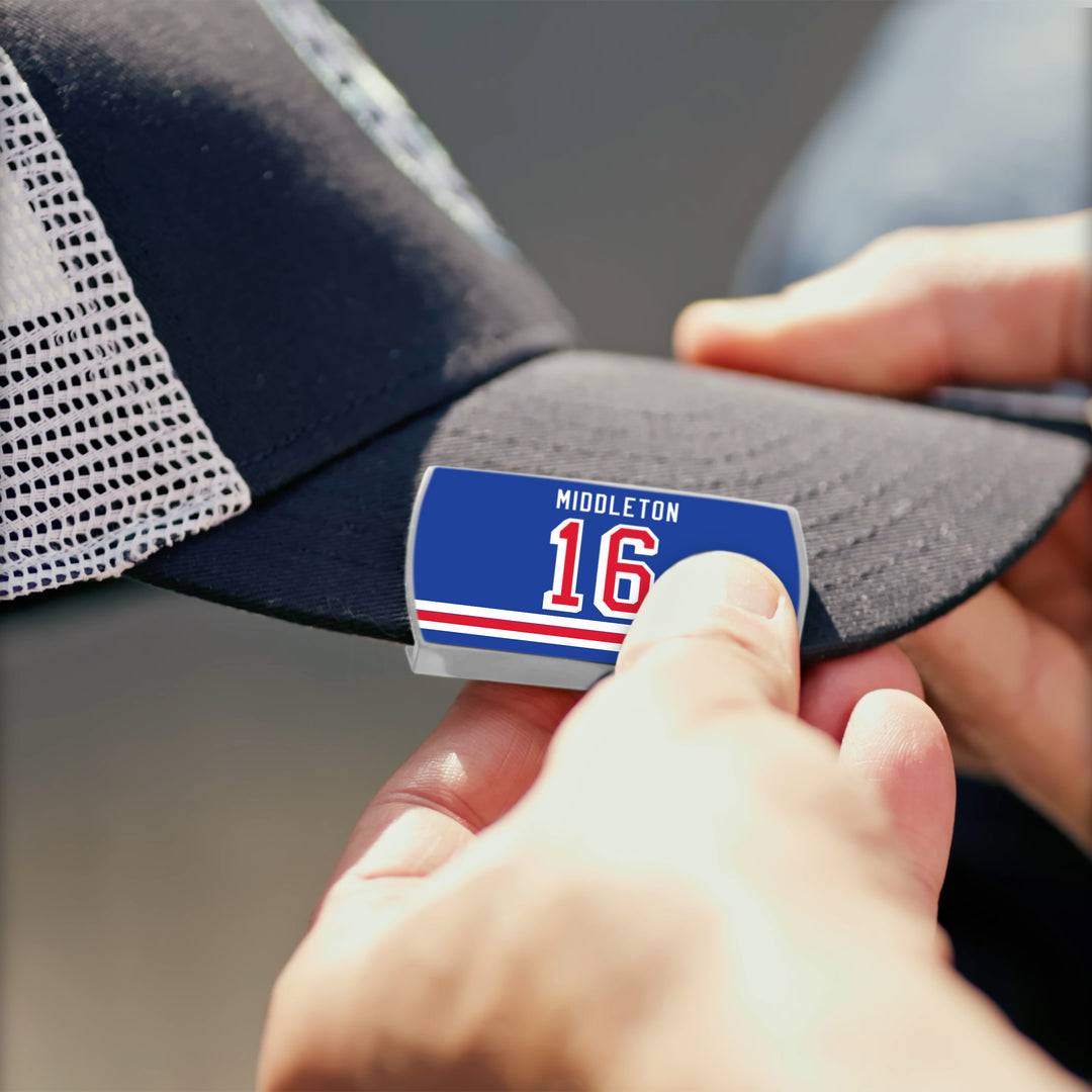 A person attaches a ZippyBack™ Rick Middleton blue badge with 16 and red-white stripes—celebrating the winger&