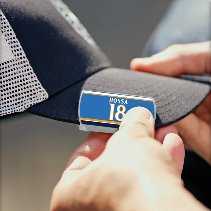 A person attaches a ZippyBack™ Marian Hossa blue and yellow label to the black brim of a mesh trucker hat, honoring Hossa&